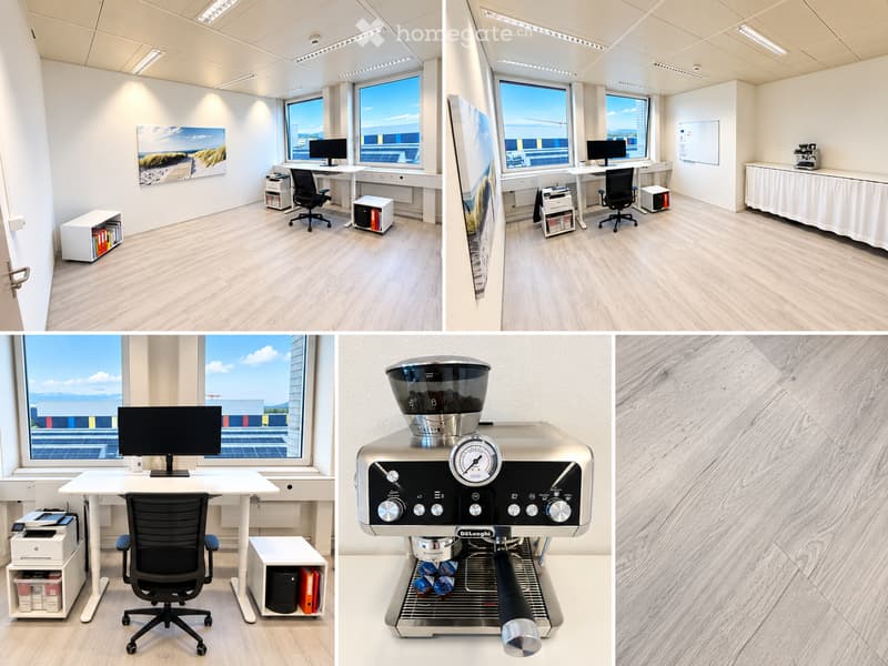Modern office space with light wood flooring, large windows, desks, chairs, computer monitors, printers, cabinets, and a coffee machine.