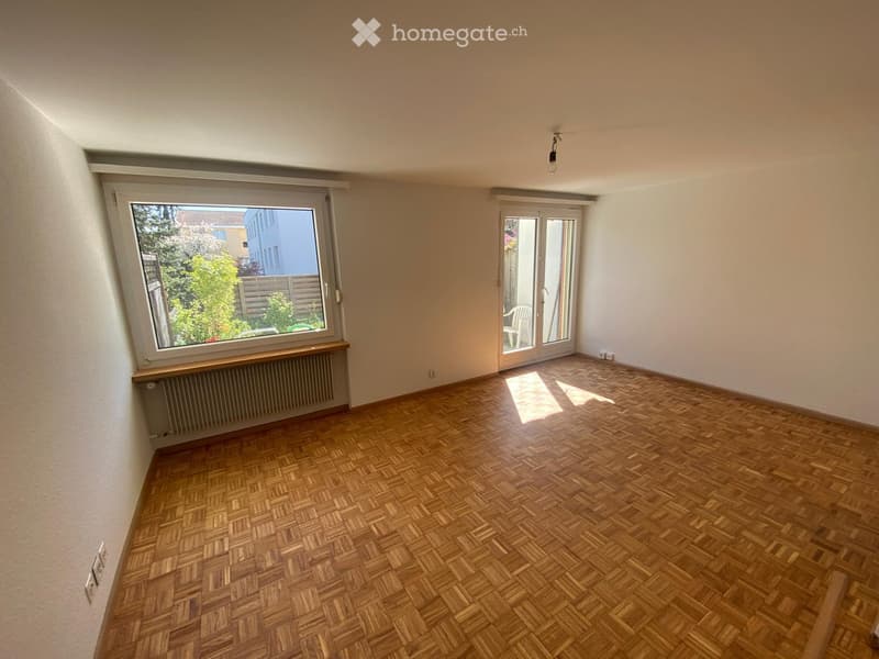 Empty room with wooden parquet flooring, large window, sliding glass door leading to a balcony, radiator, and visible electrical outlets.
