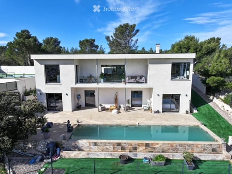 Modern two-story house with white exterior, large windows, and a swimming pool in the courtyard.