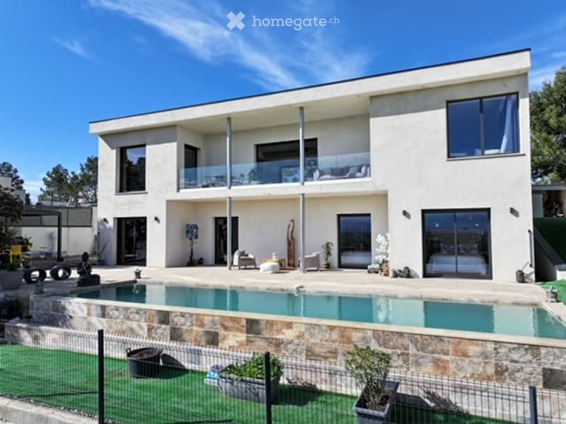 Modern two-story house with white facade, large windows, balcony, swimming pool, and outdoor seating area.