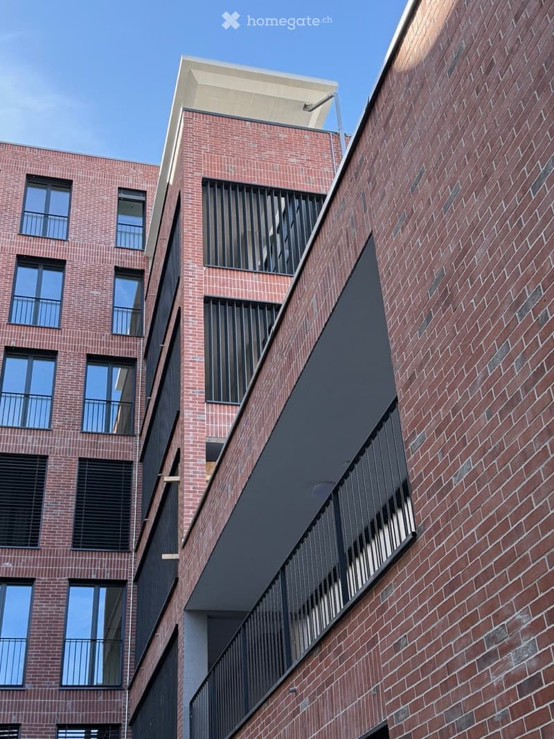 Modern multi-story brick building with large windows and balconies, featuring contemporary design elements and clean lines.