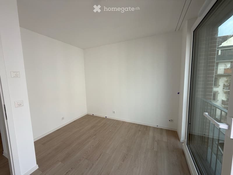Empty room with light wooden flooring and white walls, featuring a large glass door leading to a balcony.