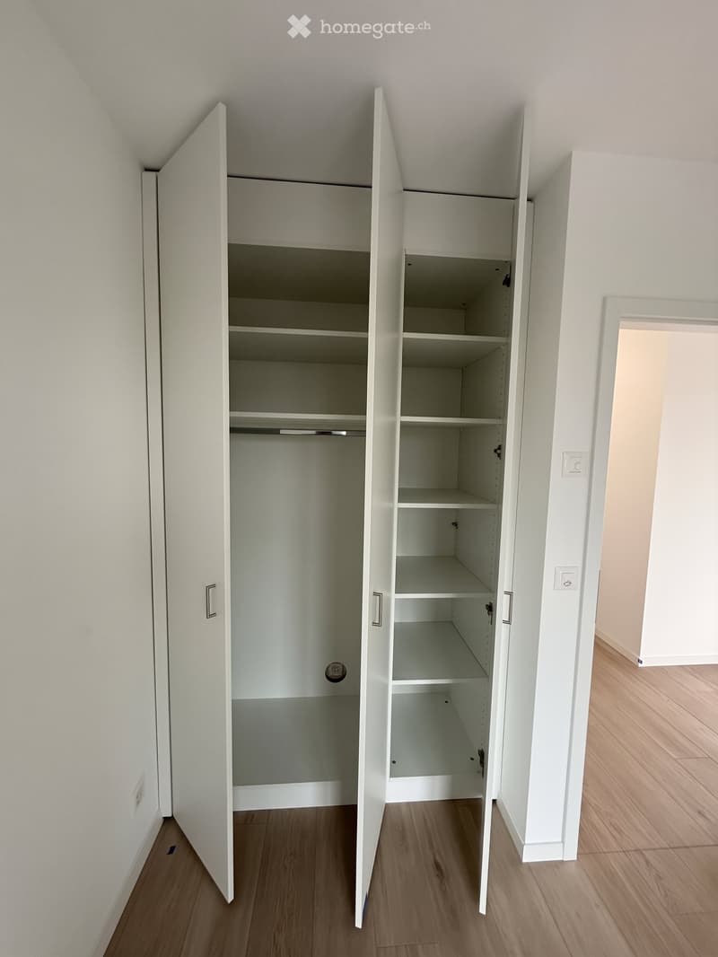 Empty room with white built-in wardrobes and wooden flooring.