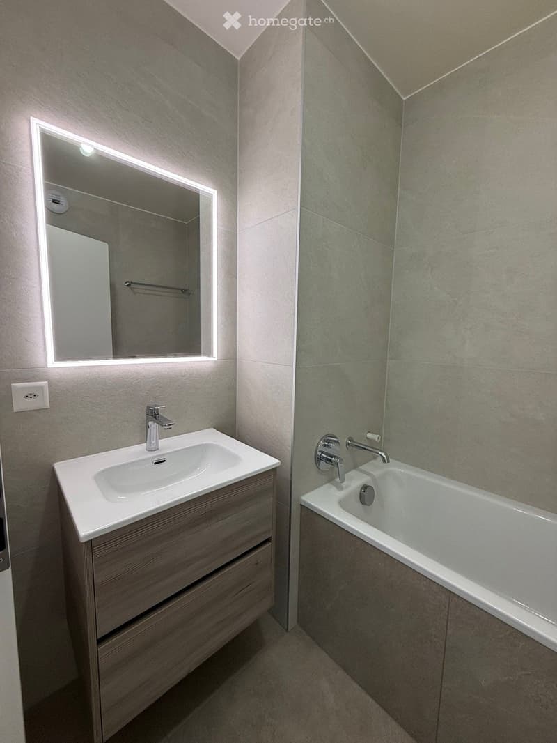 Modern bathroom with a wooden vanity, white sink, mirror with LED lighting, and a bathtub.
