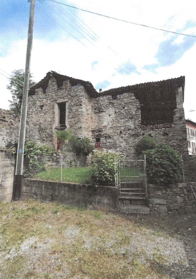 A rustic stone house with a weathered exterior, partially overgrown with vegetation, and a small staircase leading to the entrance.
