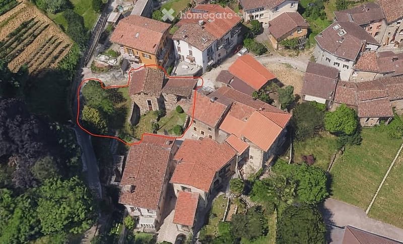 Aerial view of a cluster of traditional stone houses with red-tiled roofs, surrounded by greenery and pathways.