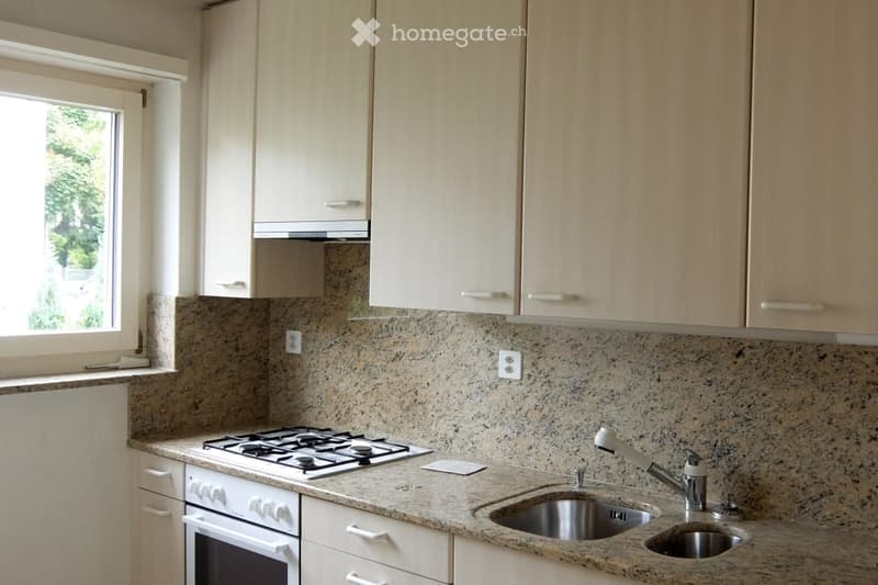 Modern kitchen with light wooden cabinets, granite countertop, gas stove, and stainless steel sink.