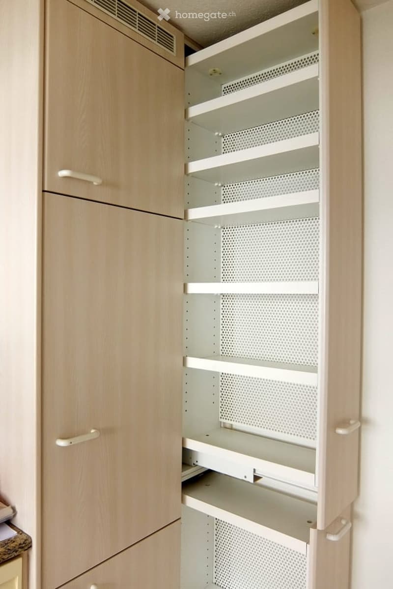Empty pantry with light wood cabinetry and open shelving units, featuring perforated metal shelves and soft-close drawers.