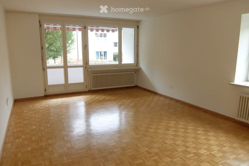 Empty room with wooden parquet flooring, large windows, and a radiator. No furniture or equipment present.