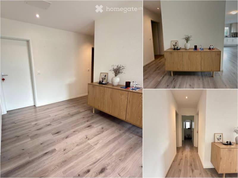 A modern hallway with light wooden flooring, white walls, and a small wooden console table with decorative items on it. The hallway leads to a bathroom and other rooms.