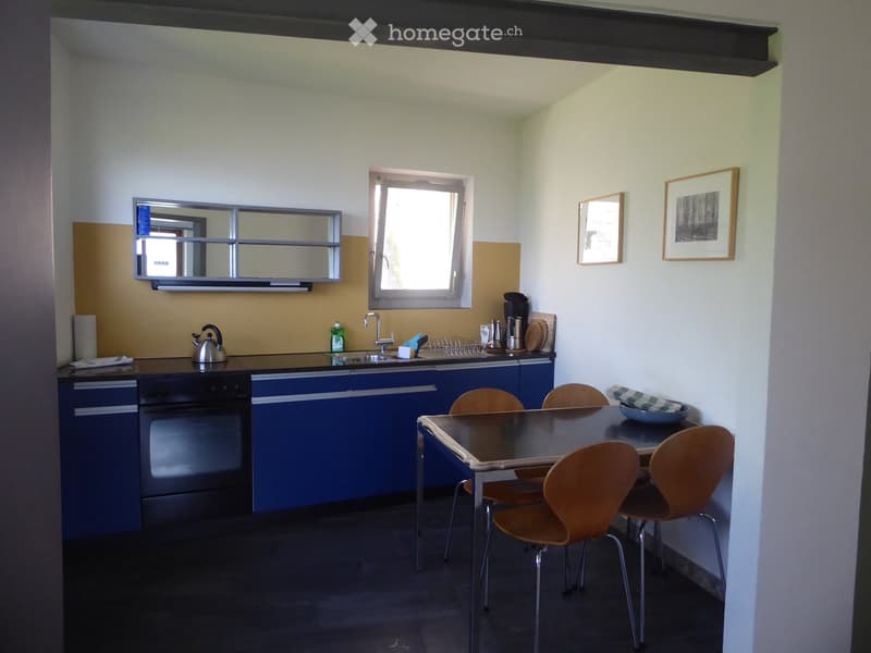 Modern kitchen with blue cabinets, black countertop, sink, oven, dining table with chairs, and a mirror above the sink.