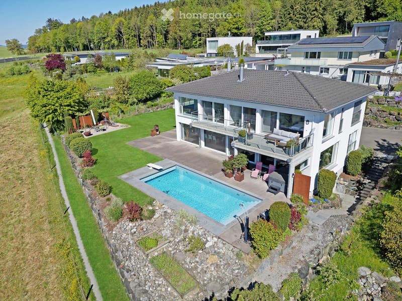 Aerial view of a modern two-story house with a large balcony, swimming pool, and well-maintained garden.