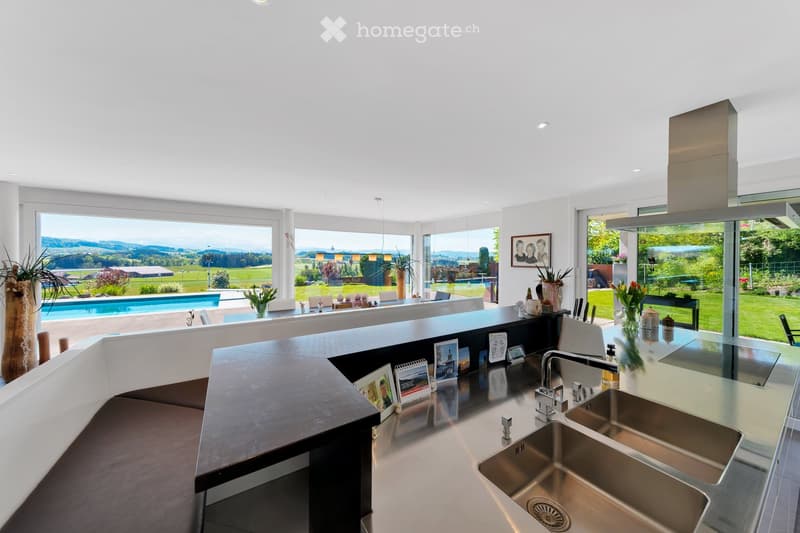 Modern kitchen with stainless steel sink, large windows offering a scenic view, and decorative items on the counter.