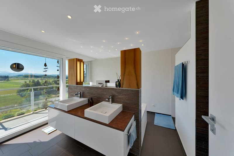 Modern bathroom with double sinks, wooden countertop, large window offering scenic view, and contemporary fixtures.