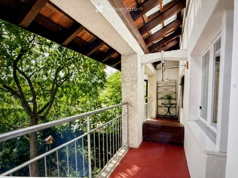 Balcony with wooden decking, red floor, white railing, and a view of greenery.