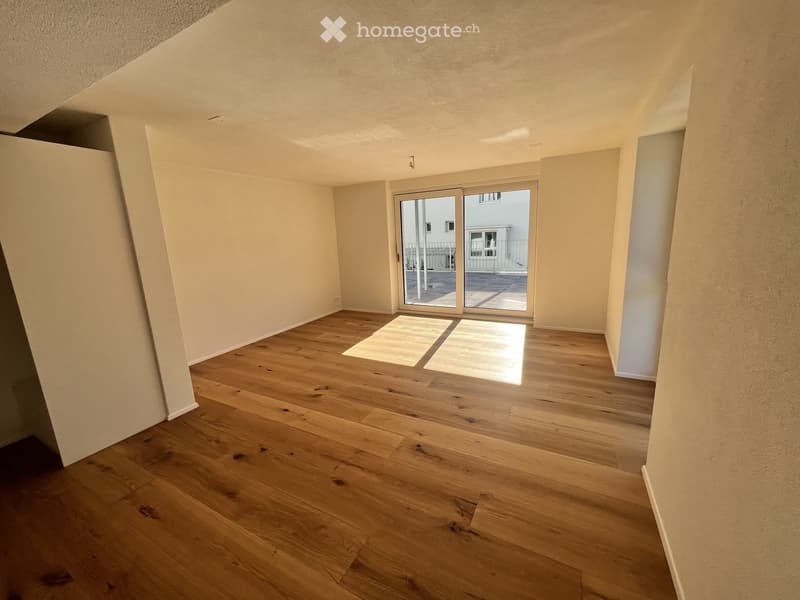 Empty room with wooden flooring, white walls, and a large sliding glass door leading to a balcony area.