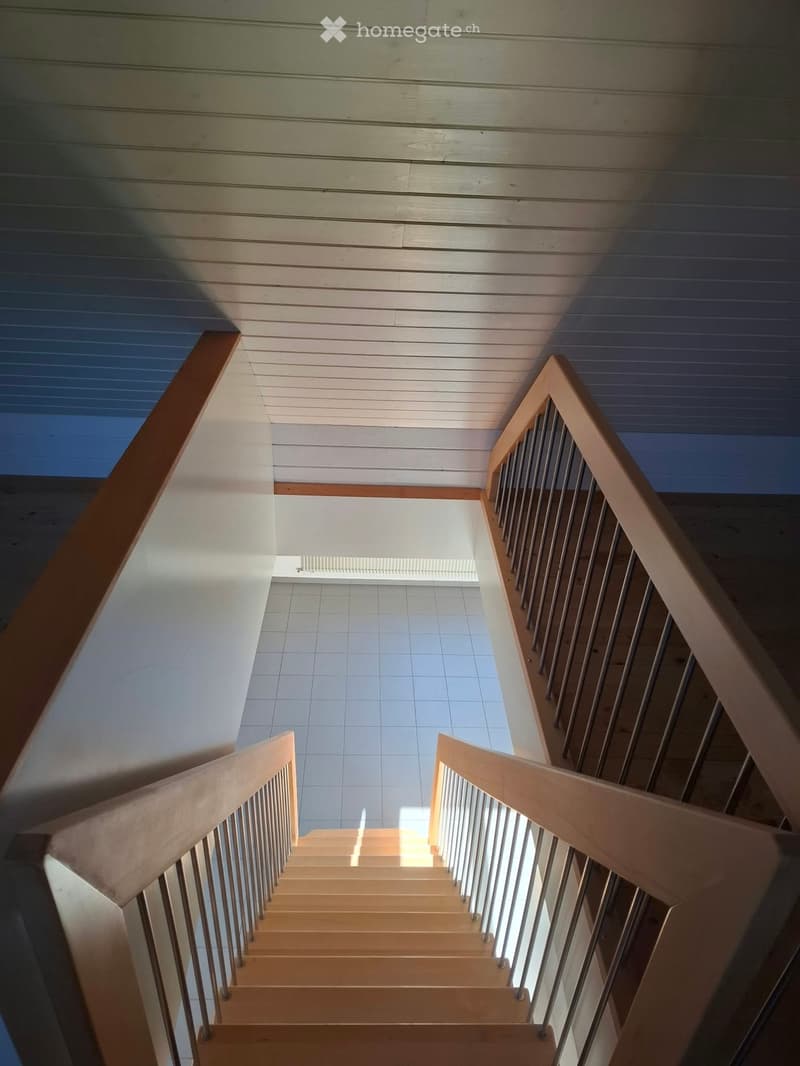 Wooden staircase with metal railings, light-colored walls, and a tiled floor below.