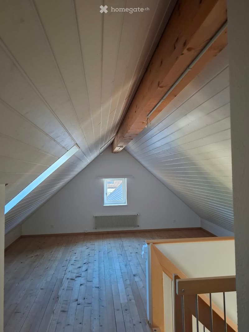 Empty attic space with wooden floors, white walls, exposed wooden beams, skylight window, and a staircase leading downwards.