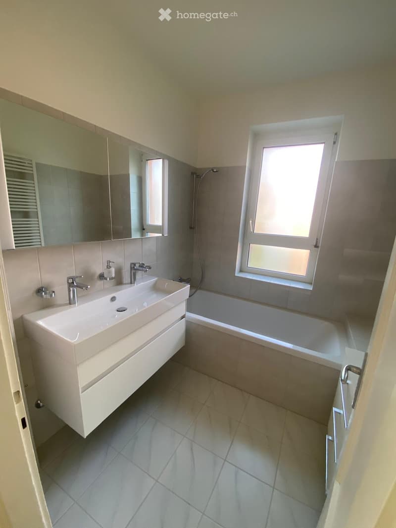 white tile flooring, white sink, large mirror, bathtub, shower, window