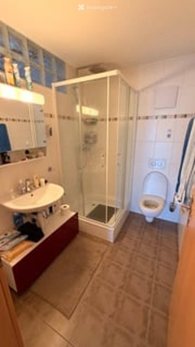 Modern bathroom with a white tiled shower, sink, mirror, and toilet. The floor is tiled in a warm beige color, and the walls are white with blue accents.