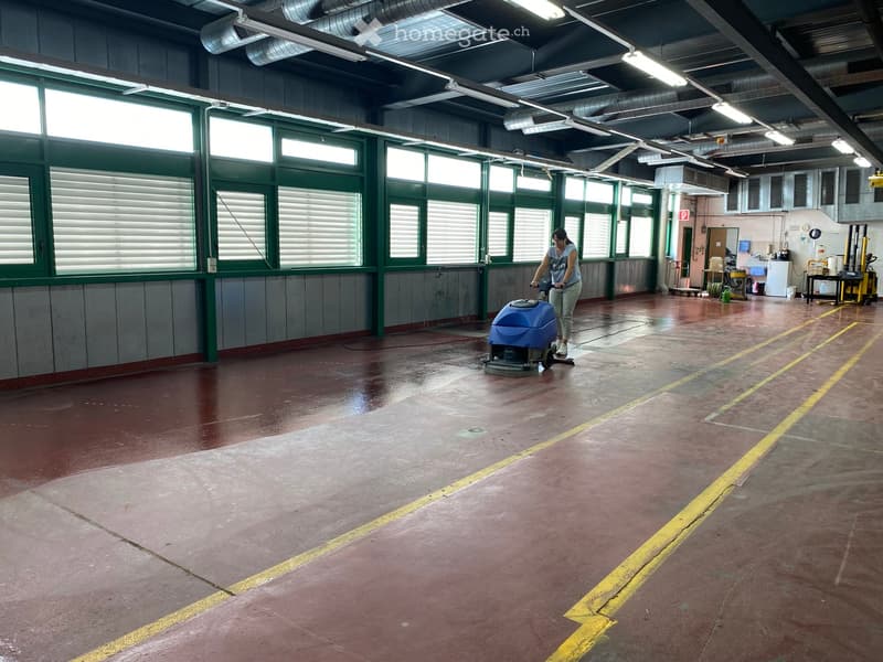 Large, empty industrial-style room with high ceilings, large windows, and a polished concrete floor. The space is clean and well-lit, with no furniture or equipment visible.