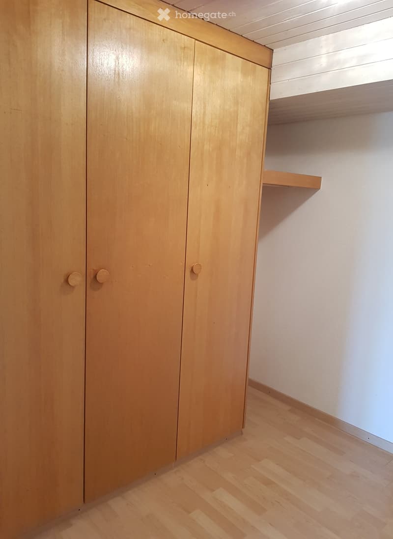 Empty room with wooden floor, white walls, and built-in wooden cabinet with two doors and a shelf above.