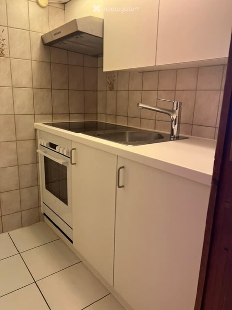 Modern kitchen with white cabinets, a built-in oven, a stainless steel sink, and a chrome faucet. The countertops are white, and the backsplash features beige tiles.