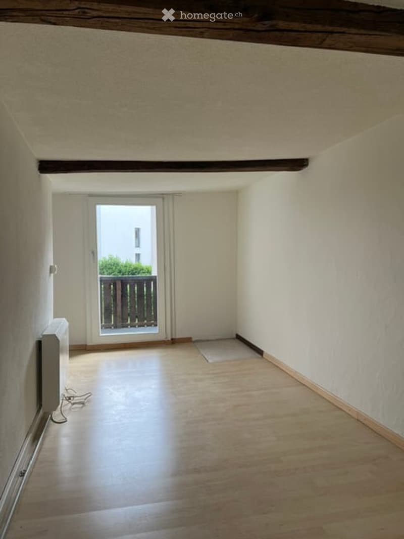 Empty room with wooden flooring, white walls, and a sliding glass door leading to a balcony.