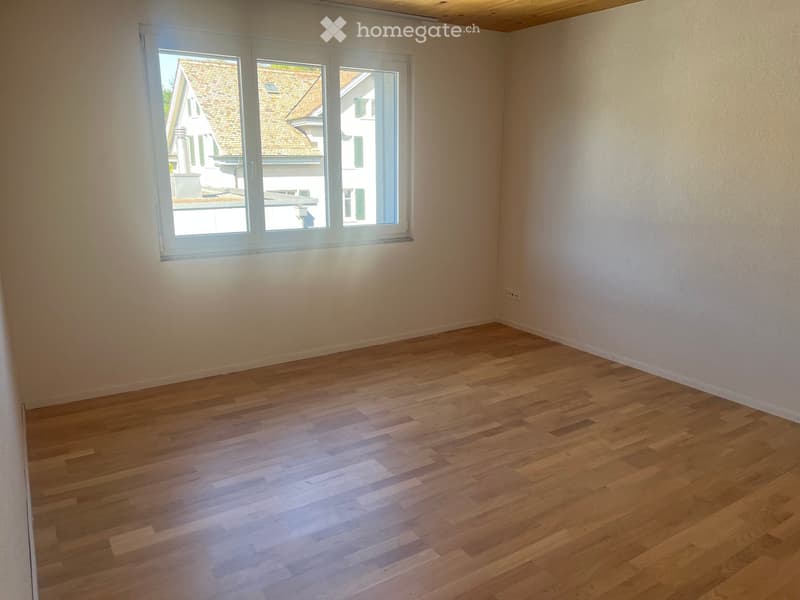 Empty room with wooden flooring and large windows letting in natural light. No furniture or equipment present.