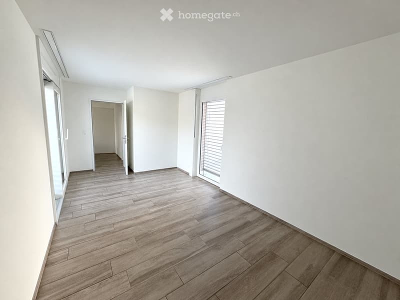 Empty room with light wooden flooring, white walls, and large windows with blinds. No furniture or equipment present.