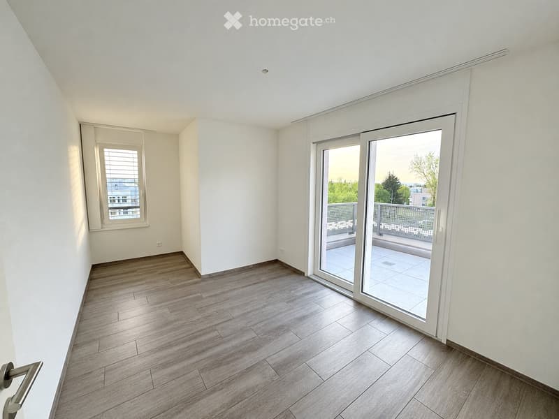 Empty room with wooden flooring, white walls, large sliding glass doors leading to a balcony, and a window with blinds.
