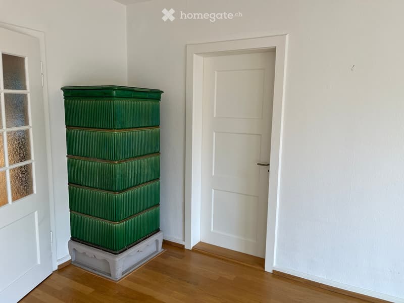A narrow hallway with wooden flooring, white walls, and a green radiator stacked against the wall. Two white doors are visible, one on each side of the hallway.