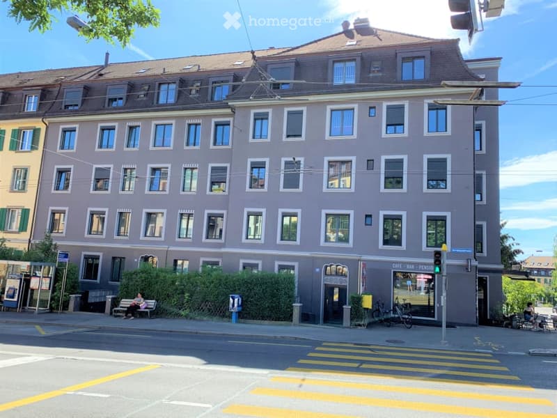 Four-story residential building with multiple windows, grey facade, and a ground-floor cafe entrance.