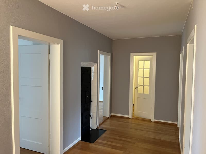 Empty hallway with wooden flooring, grey walls, and multiple doors leading to other rooms.