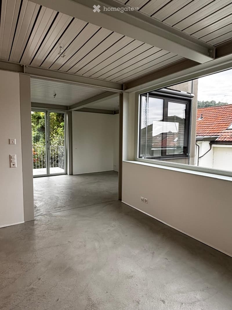 Empty room with concrete floor, large windows, and sliding glass doors leading to a balcony.