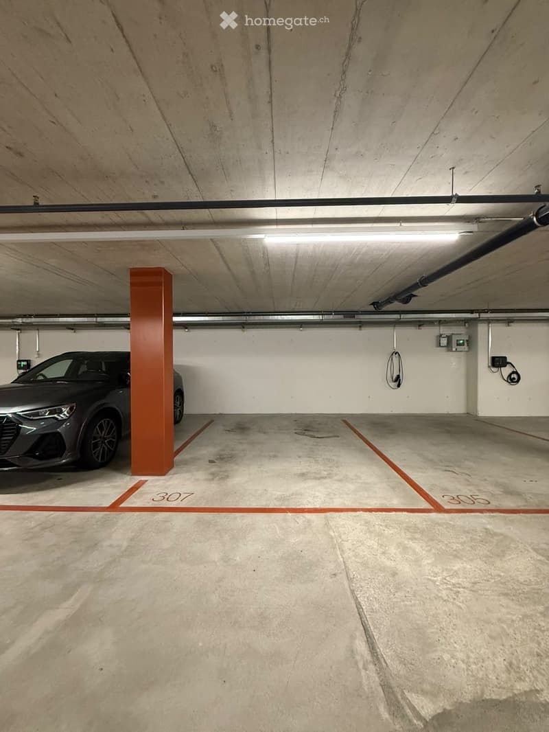 Underground parking space with concrete floors and walls, marked parking spots, and a single parked car.