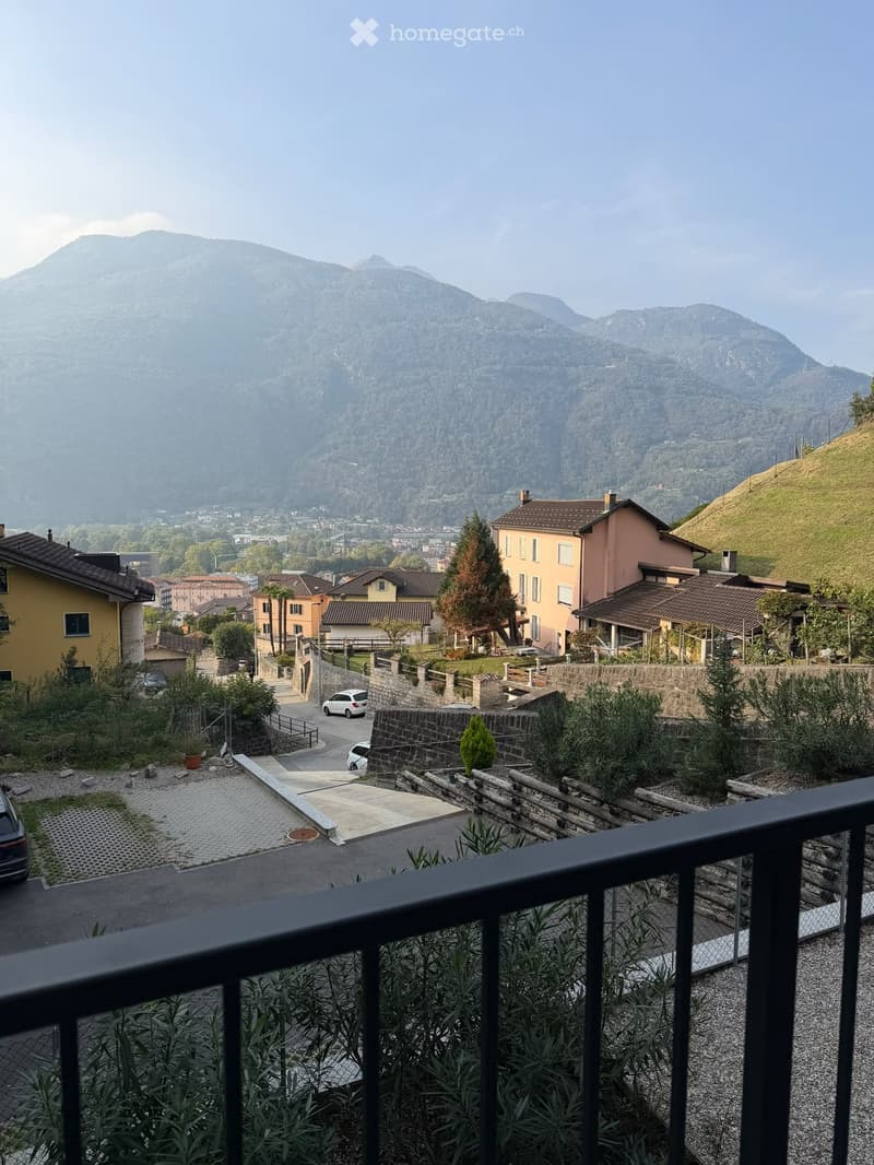 Balcony overlooking a scenic town with houses, a stone wall, and distant mountains.