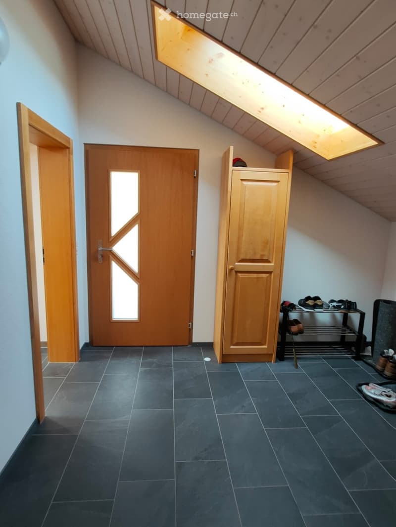 A narrow hallway with dark tiled flooring, wooden doors, and built-in wooden cabinetry. The ceiling has exposed wooden beams and a skylight. A small shoe rack is visible on the right side.