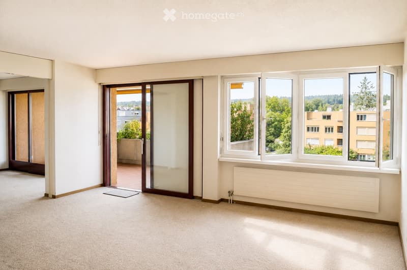 Empty room with light-colored walls, carpeted floor, large windows, and a sliding glass door leading to a balcony.
