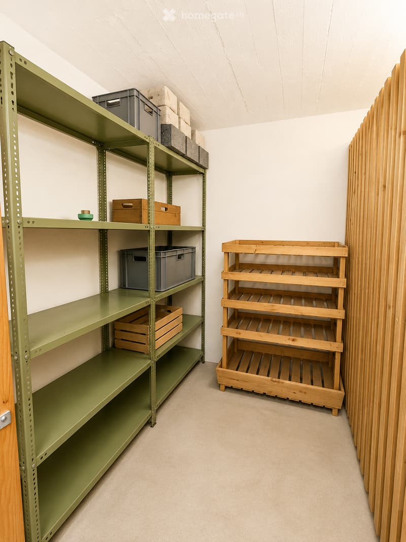 Empty storage room with green metal shelving unit and wooden shelving unit, both partially filled with boxes and containers.