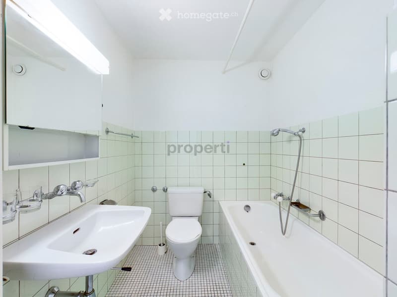 Modern bathroom with white tiles, a sink, toilet, bathtub, and a mirrored cabinet above the sink.