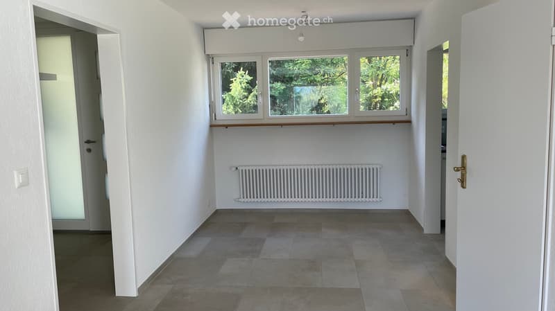Empty room with tiled floor, white walls, large window with wooden sill, radiator, and two doors.