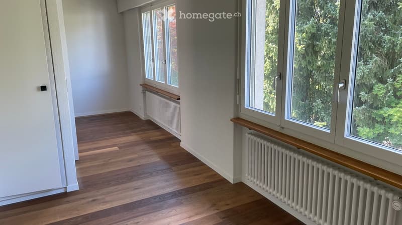 Empty room with wooden flooring, large windows, radiators, and wooden window sills.