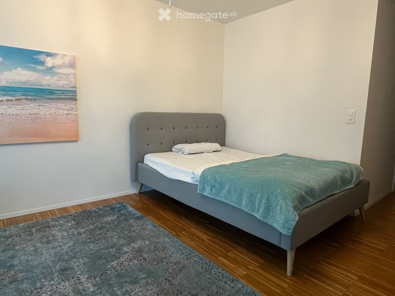 Cozy bedroom with a single bed, grey headboard, blue blanket, and a large beach-themed picture on the wall.