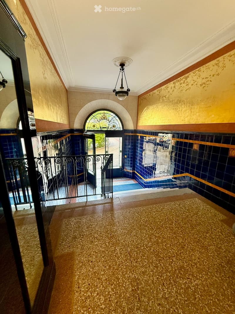 Staircase with ornate metal railing, decorative tilework, and stained-glass window at the top.