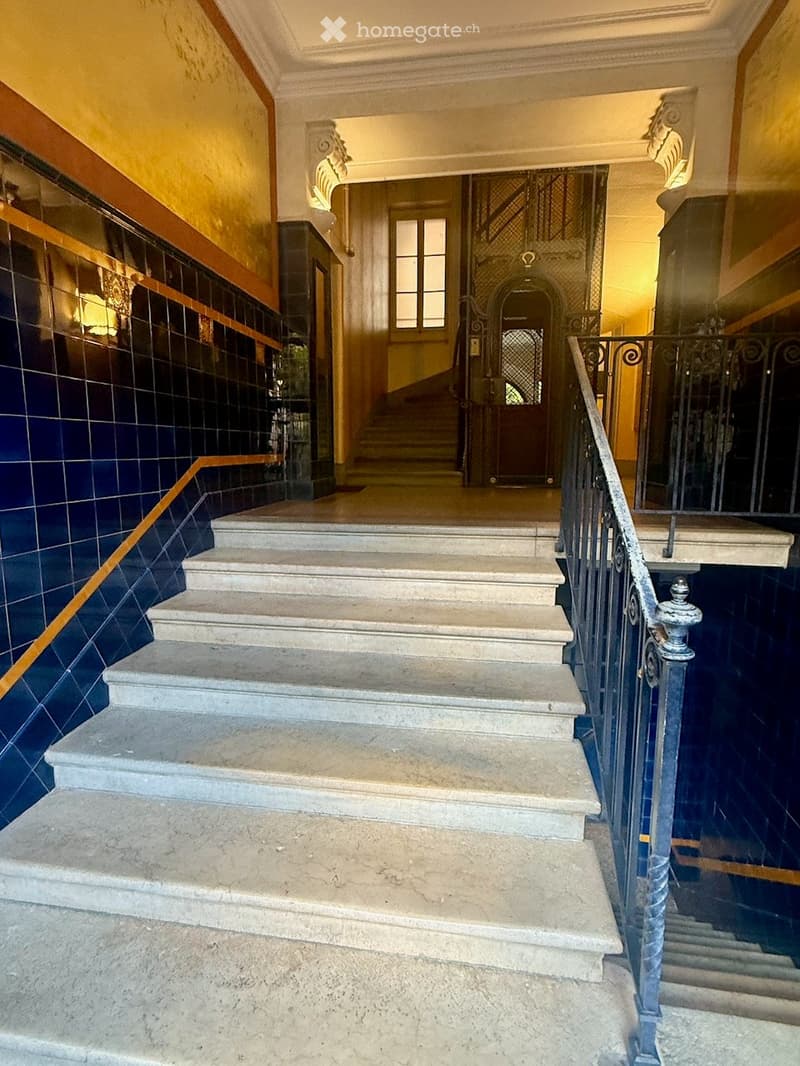 Staircase with ornate metal railing, marble steps, and decorative wall tiles leading to an arched doorway.