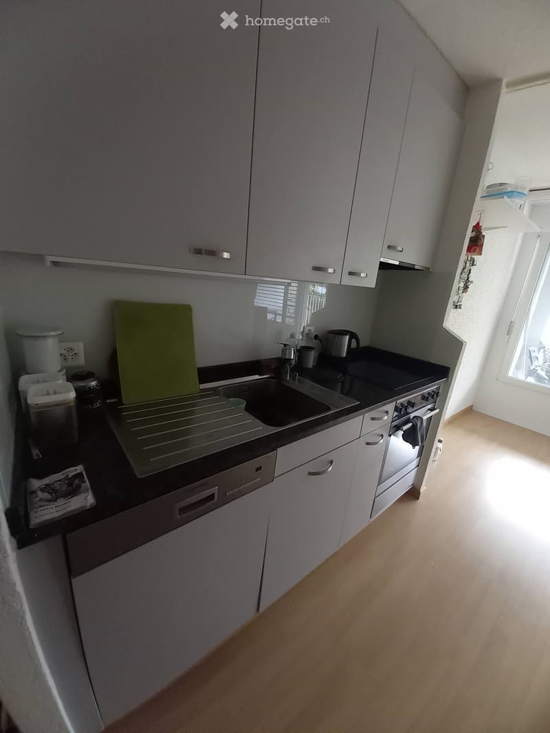 Modern kitchen with white cabinets, black countertops, stainless steel appliances, and a sink with a faucet. Includes a coffee maker, cutting board, and various small items on the counter.