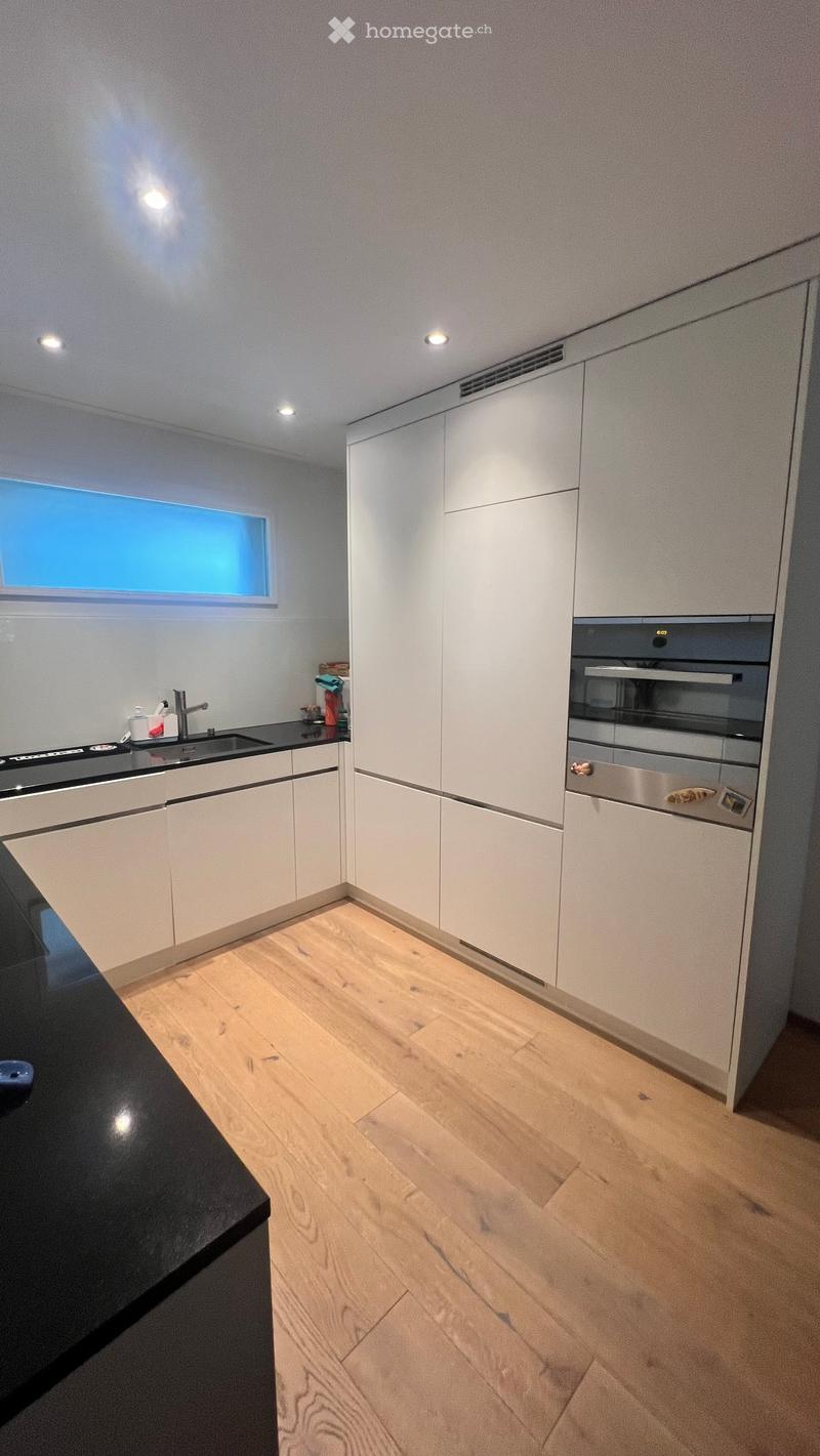 Modern kitchen with white cabinets, wooden flooring, and a black countertop. Features include a sink, faucet, and built-in oven.