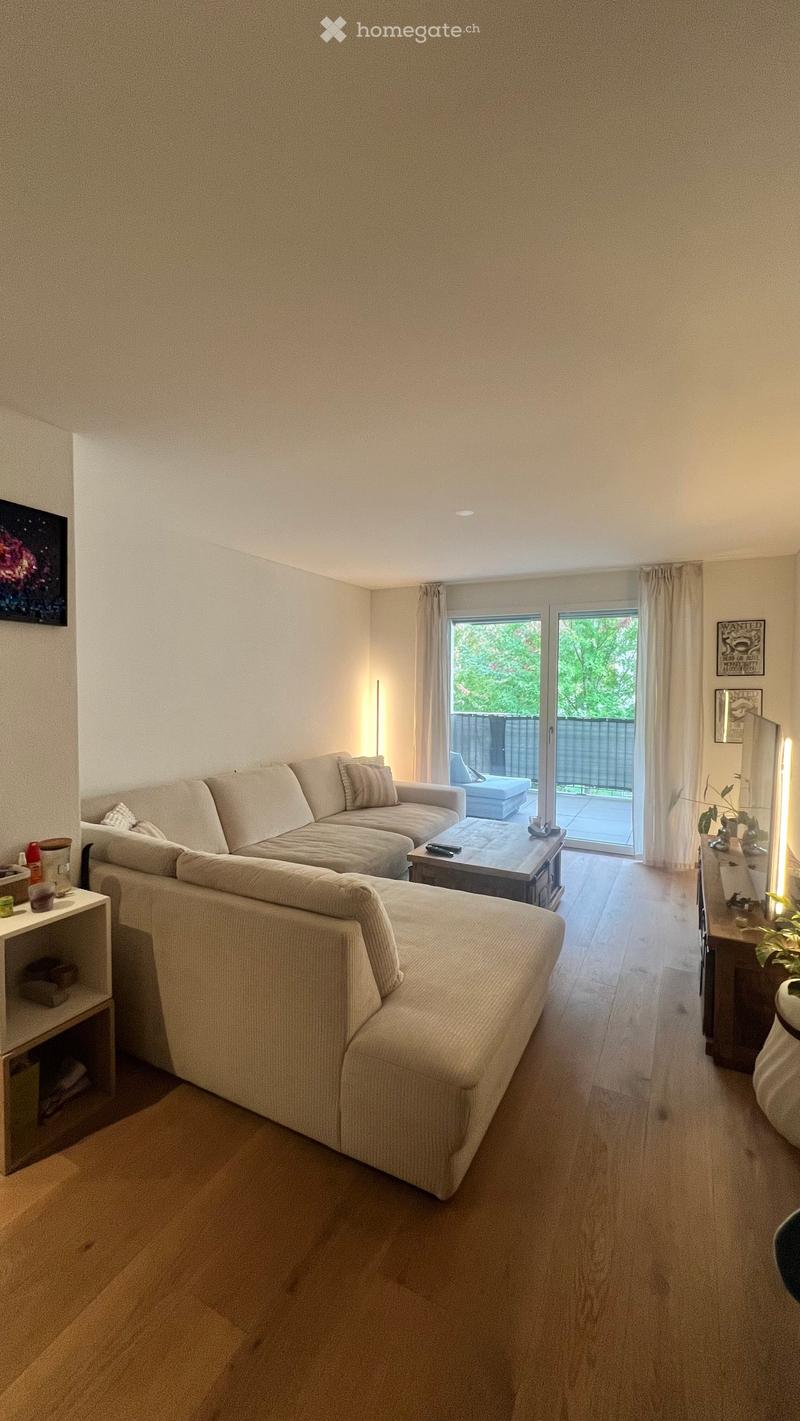 Modern living room with a large sectional sofa, coffee table, side table, and a view of a balcony through large glass doors.
