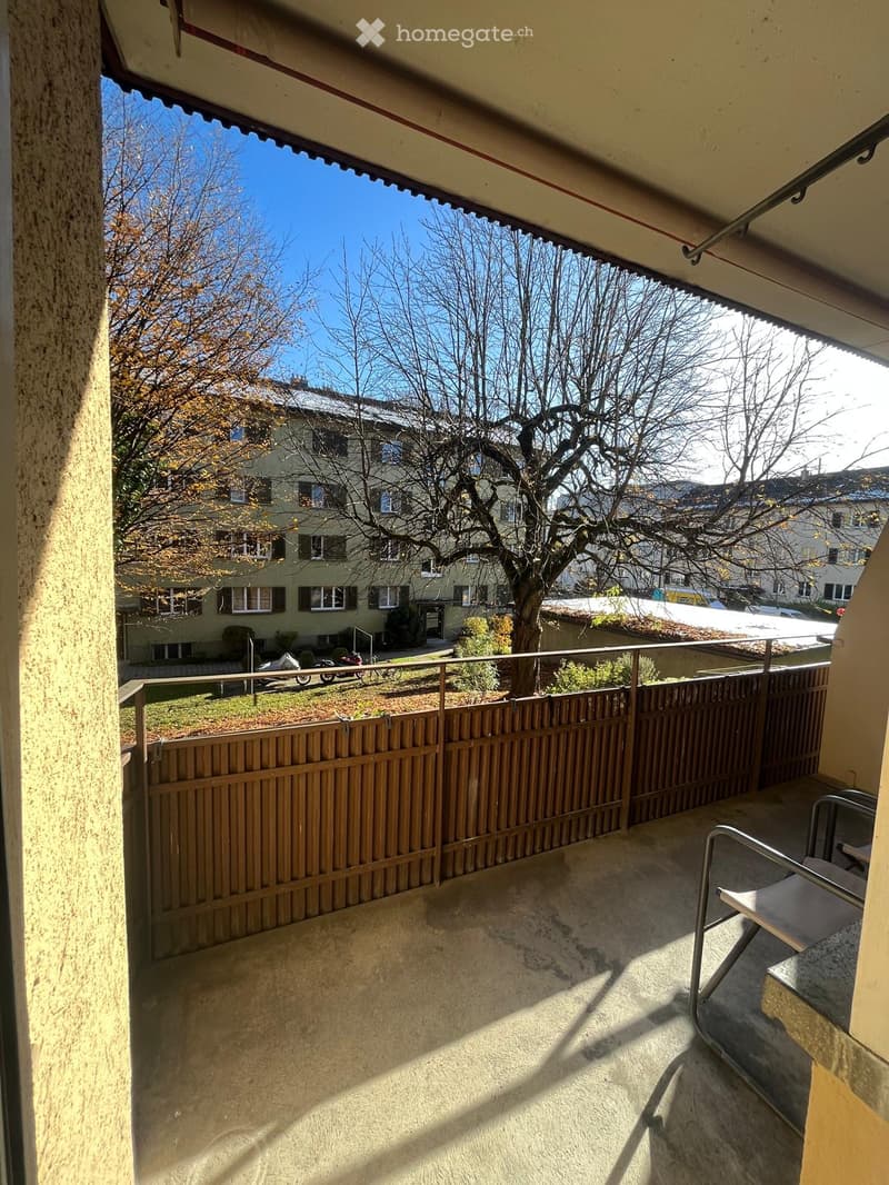 Balcony with a wooden fence, a single chair, and a view of a residential area with trees and houses.